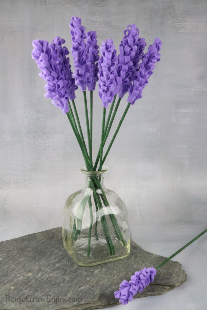 Glass bottle full of lavender felt flowers sitting on slate