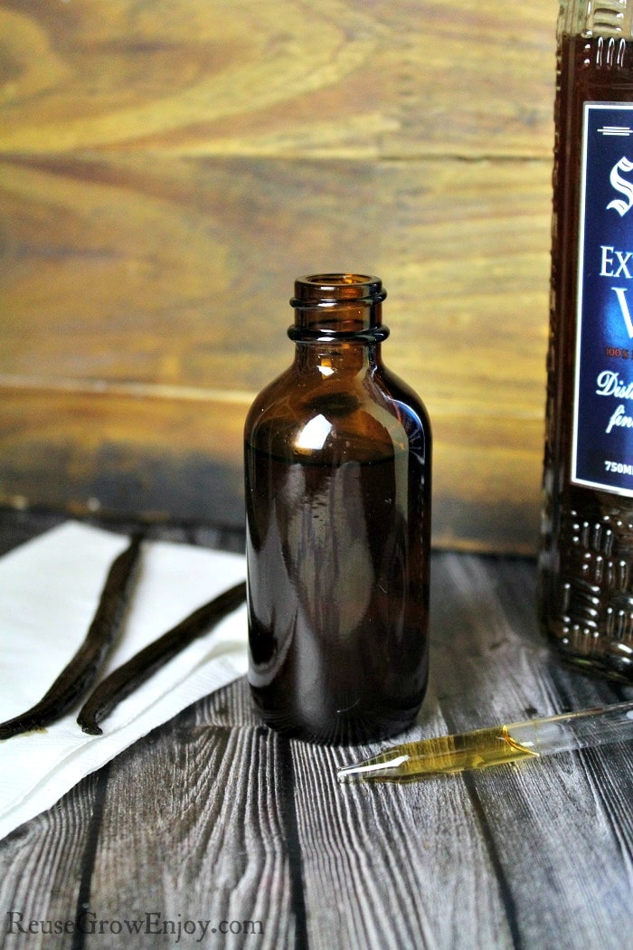 Small brown bottle full of homemade vanilla extract with vanilla beans on the left side.