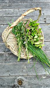 A flat basket with fresh cut herbs in it sitting on natural wood boards.