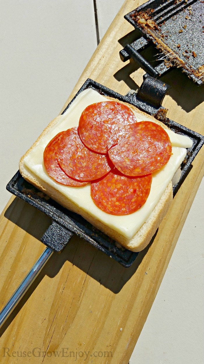 Bread in pie iron with pepperoni and cheese on it.