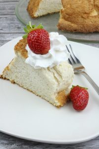 Slice of angel food cake on white plate with rest of cake in background