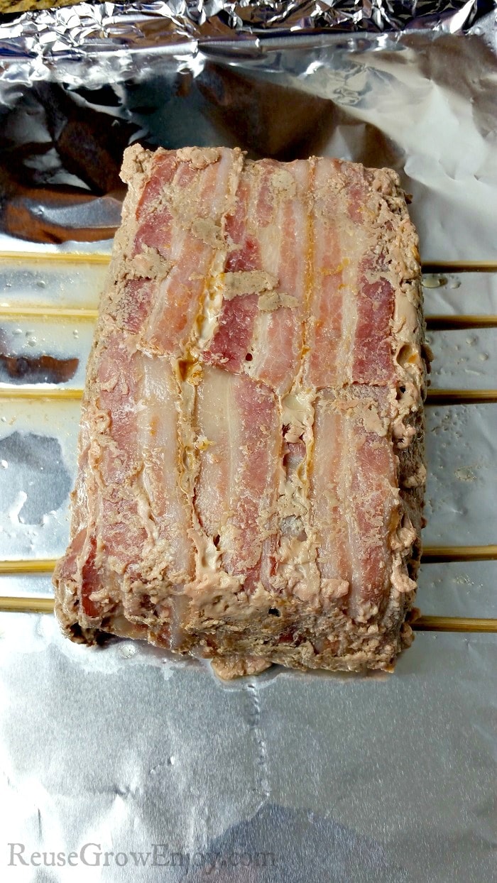 Cooked bacon wrapped Whole30 meatloaf on a foil covered cookie sheet on wooden skewers. 
