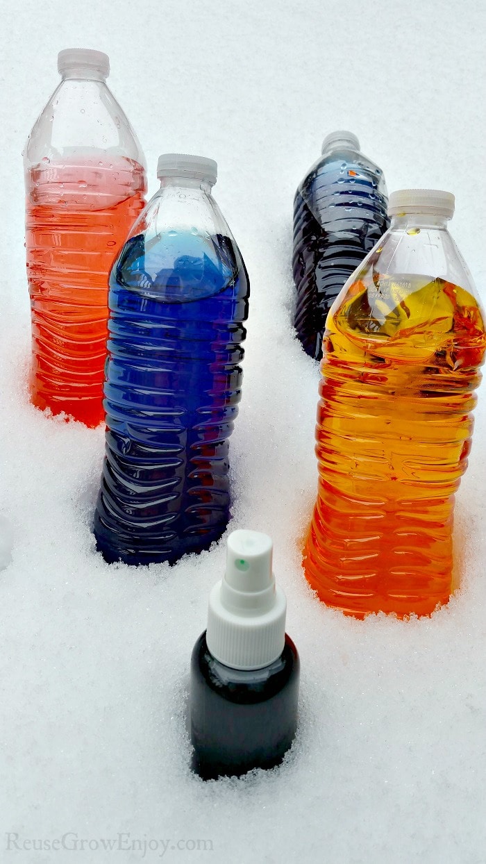 Water bottles with food coloring mixed snow paint in them sitting on snow.