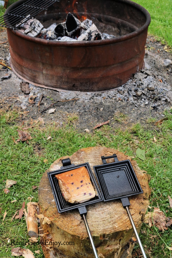 Muffin in pie iron on a stump with campfire in background