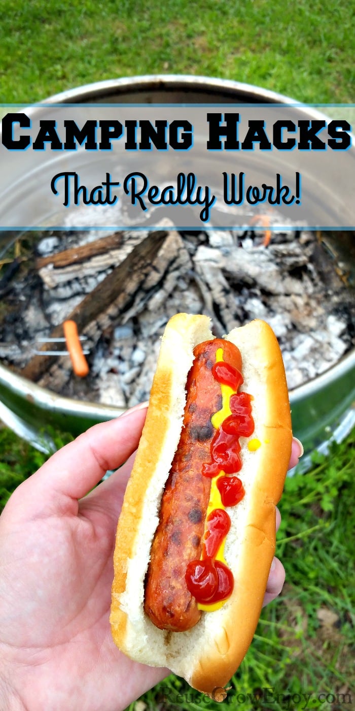 Hand holding a hot don on a bun with ketchup and mustard campfire in background. Text overlay that says Camping Hacks The Really Work.