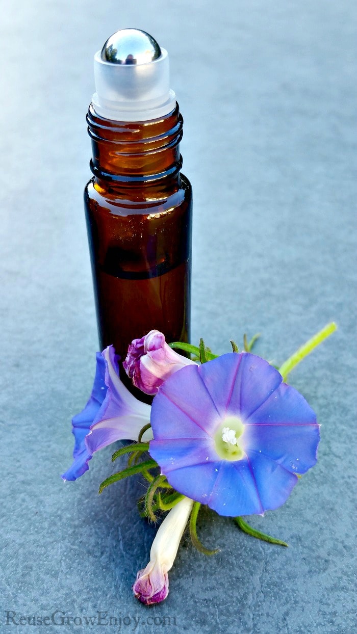 Small brown essential oil roller bottle with purple flowers laying in front.