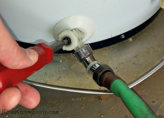 Hand turning screw driver to open water valve on hot water heater