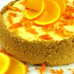 A whole orange cheesecake on a white plate with orange slices that look like a flower on the top.