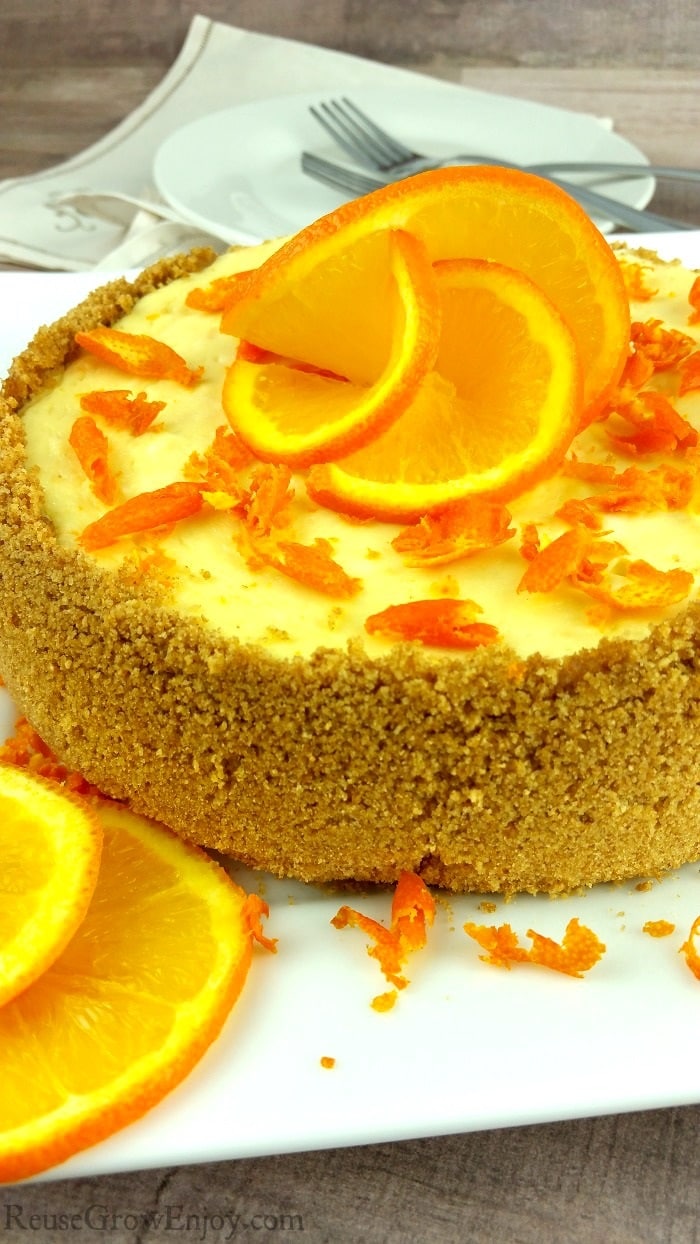 A whole orange cheesecake on a white plate with orange slices that look like a flower on the top.