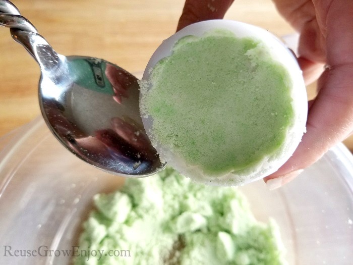 Spoon pressing green bath bomb mixture into the press mold.