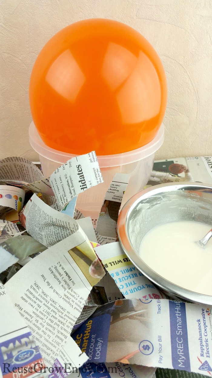 Orange balloon, newspaper in strips and bowl of paper mache paste.