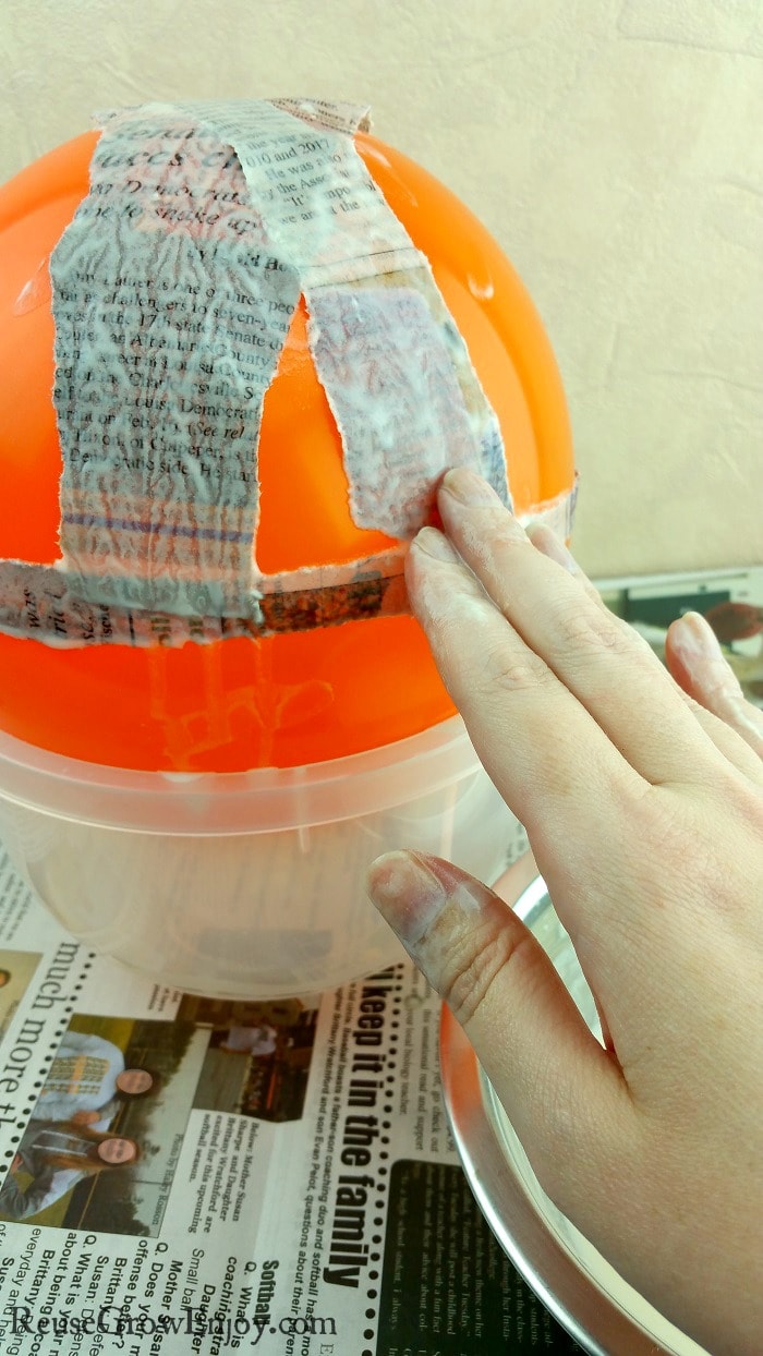 Hand layering newspaper pieces over balloon for paper mache.