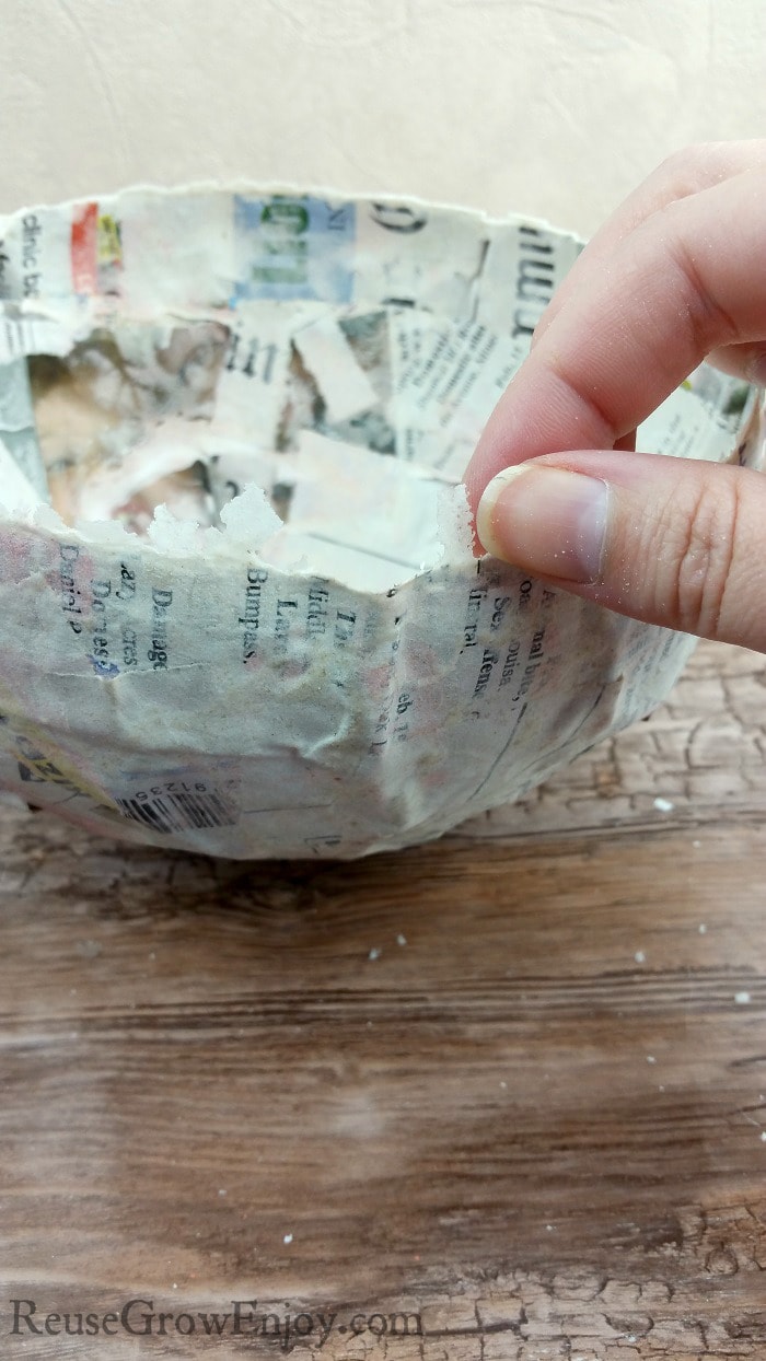 Hand pinching off dried paste from edge of paper mache bowl.