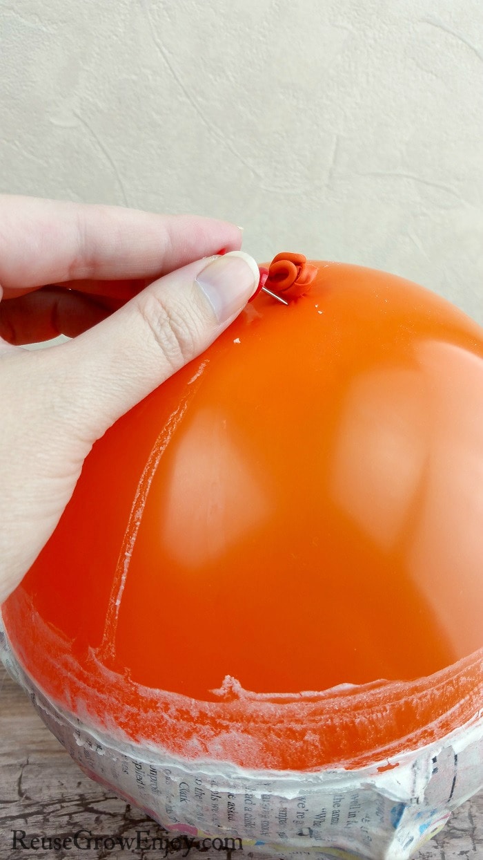 Hand holding push pin making a hole at the tip of the balloon