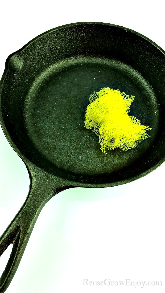 Black cast iron pan with yellow mesh produce bags made into scrubber laying in pan