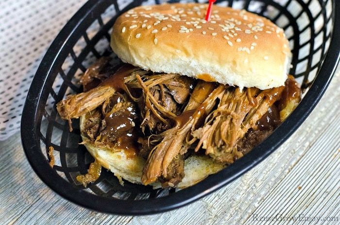 Pulled pork sandwich on a bun sitting in a black plastic basket with a wood background.