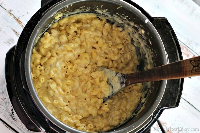 Pressure cooker mac and cheese in the pot being mixed with a wood spoon.