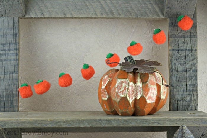 Finished pumpkin fall garland hanging on barn wood shelf with pumpkin decor in front.