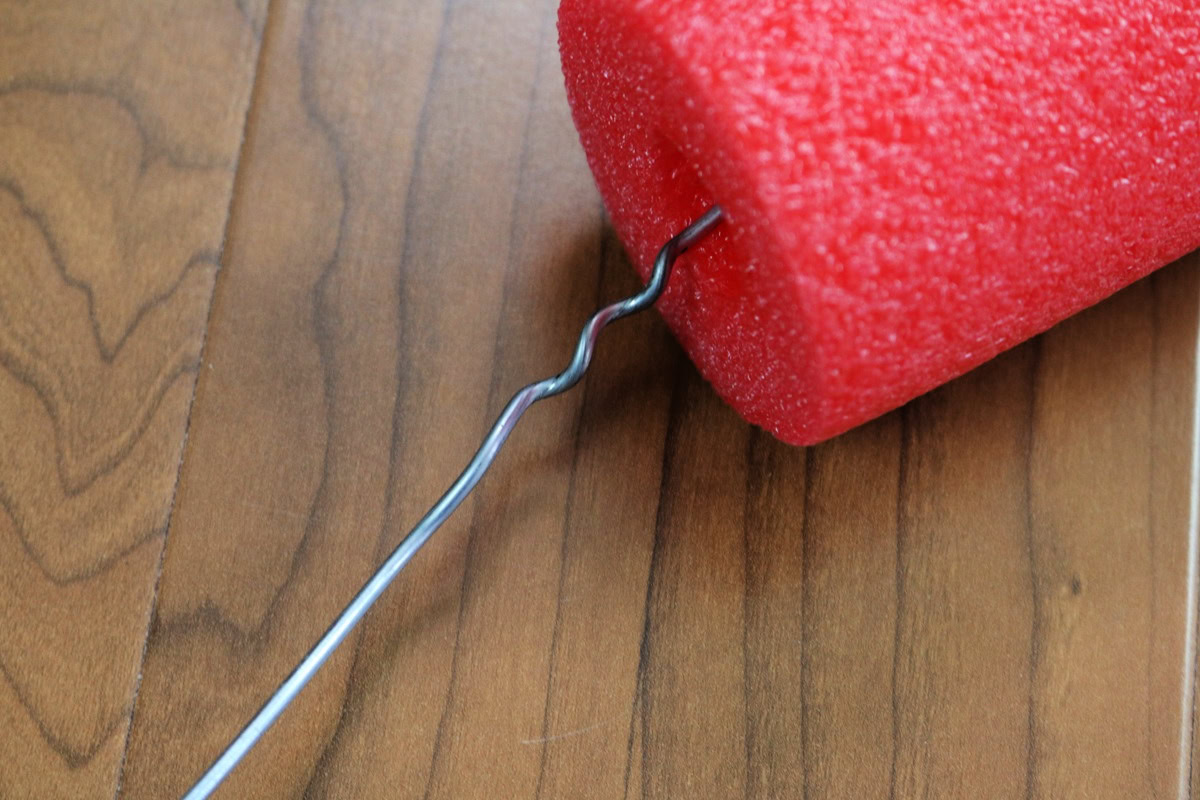 Close-up of a red pool noodle with a metal hook for crafting a giant candy cane.