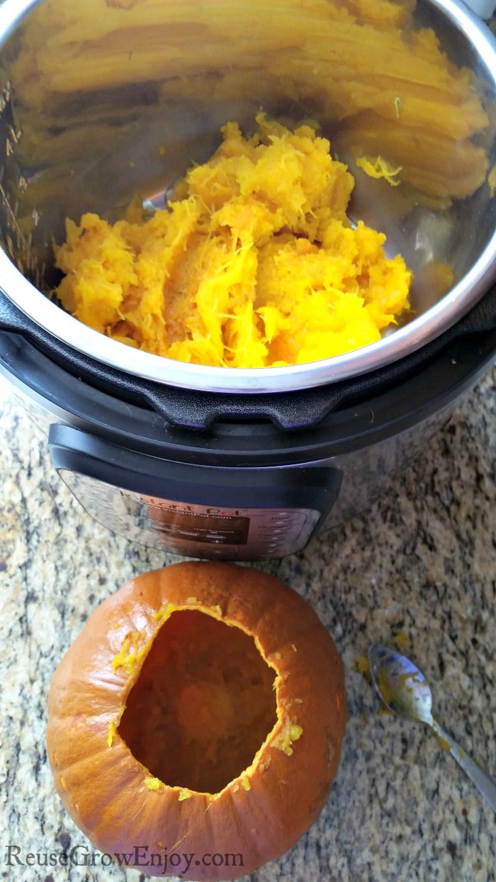 Cooked pumpkin inside of a Instant Pot with the scooped out shell in front and a spoon beside it.
