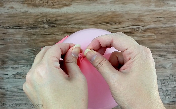 Two hands holding a pink balloon and putting a hole in the balloon with a pushpin. 