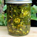 Glass jar full of Candied Jalapenos green plants in background.