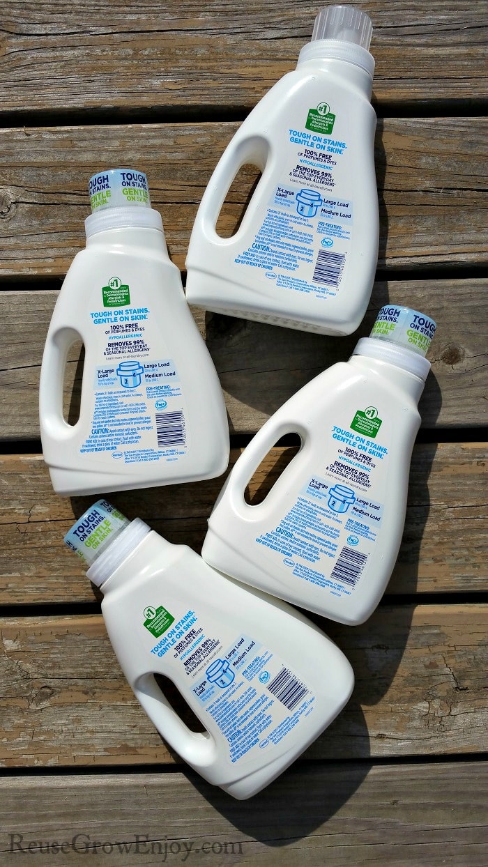 Four white laundry detergent bottle laying flat on wood deck boards.