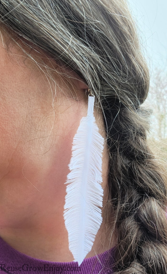 Ribbon feather earring on ear with braided hair to the side