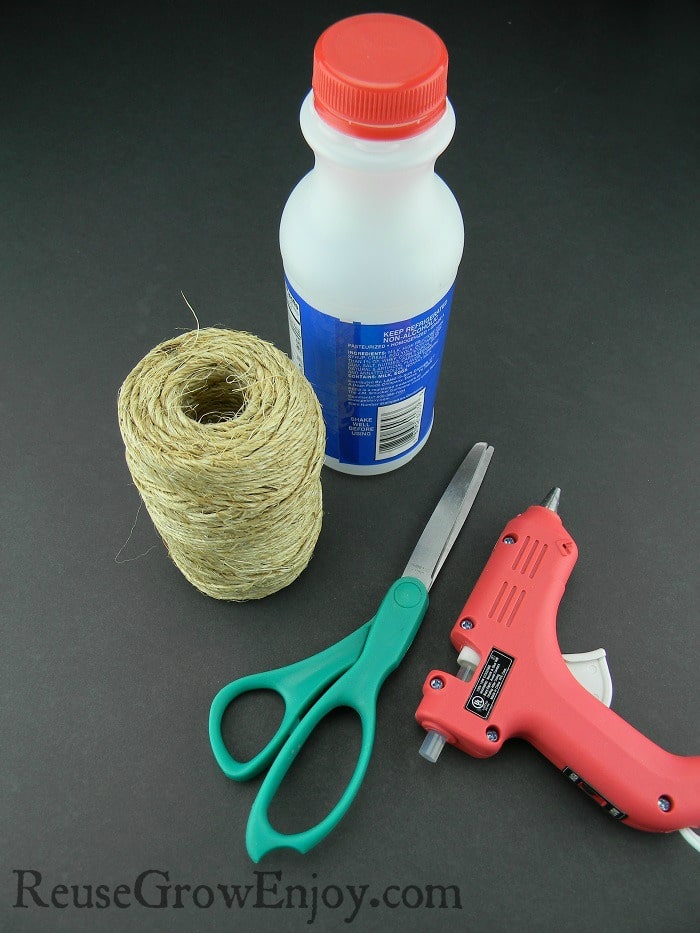 Empty plastic small milk bottle, scissors, glue gun and twine on black background