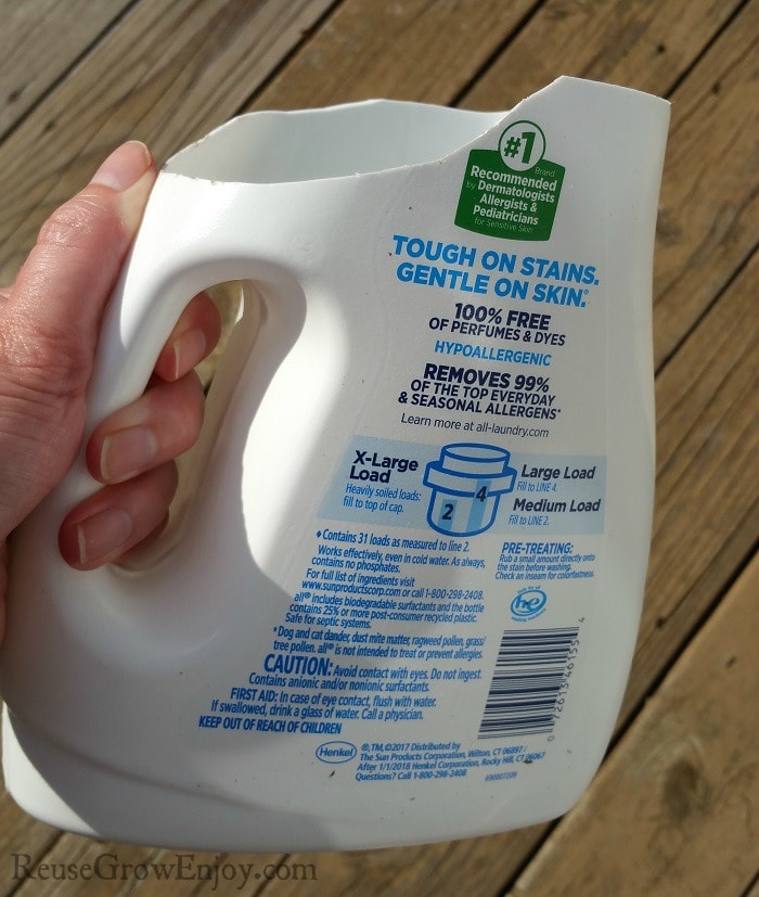 A hand holding a Scoop Made From Detergent Bottle with wood boards in the background.