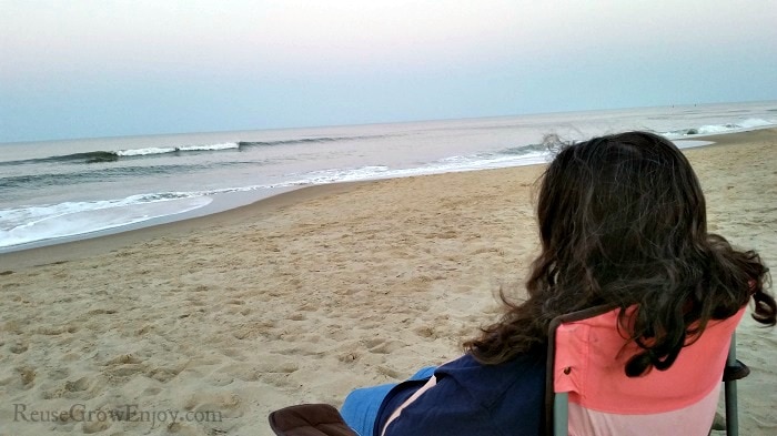 Women sitting in chair on beach looking at ocean.