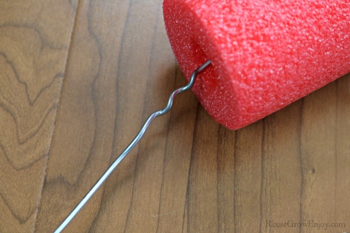 Coat hanger being pushed through red pool noodle