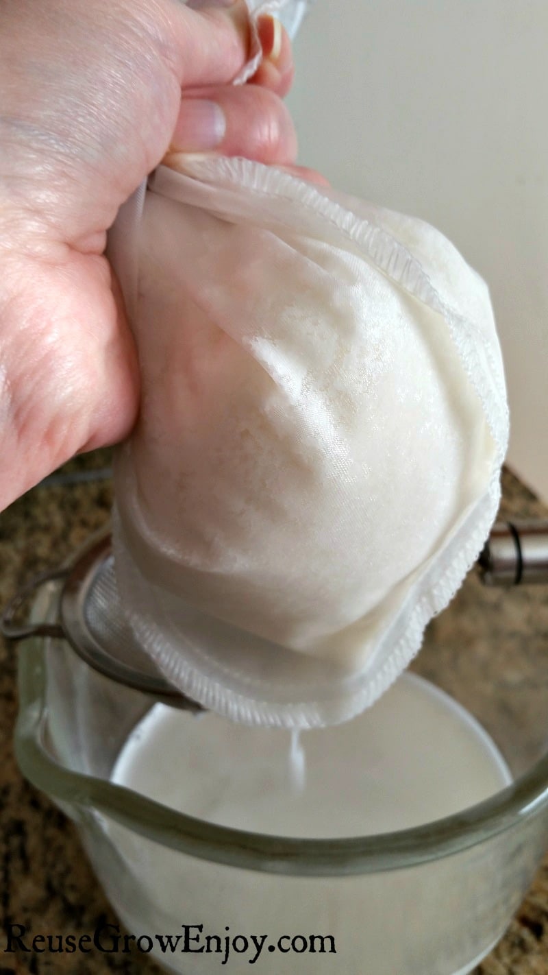 Hand squeezing nut bag over strainer into a glass cup