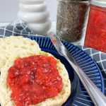Strawberry jam on a english muffin on blue plate with jar of jam in background