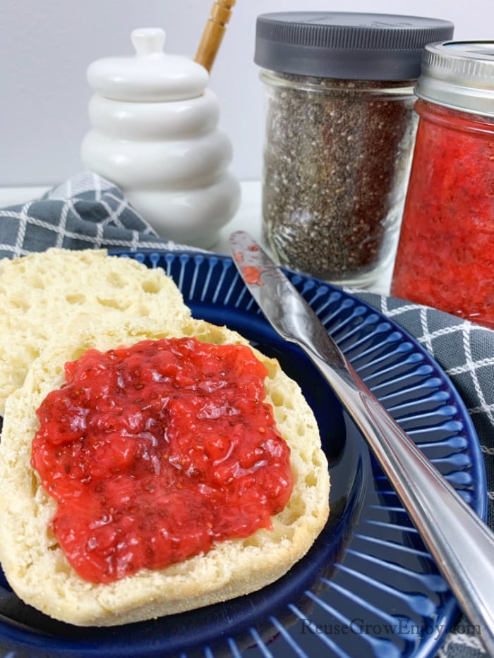 Strawberry jam on a english muffin on blue plate with jar of jam in background