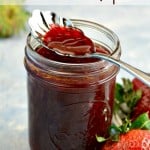Jar of homemade strawberry vinaigrette dressing with a spoon dipping into top of jar fresh strawberries to the side of jar text overlay at the top
