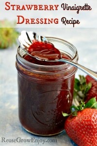 Jar of homemade strawberry vinaigrette dressing with a spoon dipping into top of jar fresh strawberries to the side of jar text overlay at the top