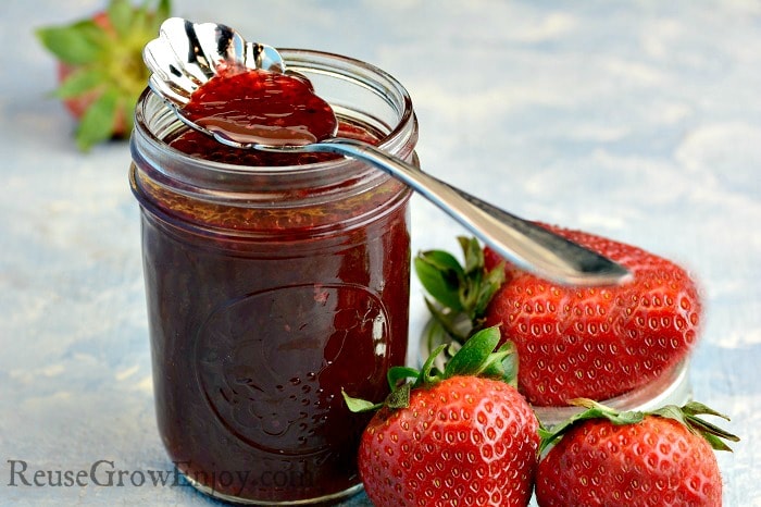 Jar of homemade strawberry vinaigrette dressing with a spoon dipping into top of jar 3 fresh strawberries to the side of jar