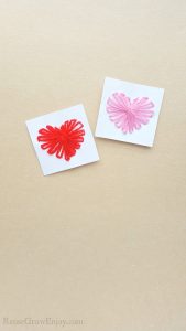 String heart craft made on white cardstock paper one heart has pink thread the other has red. Both laying on a brown paper background.
