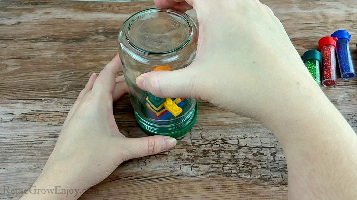 Hand placing empty jar over LEGO stack on lid.