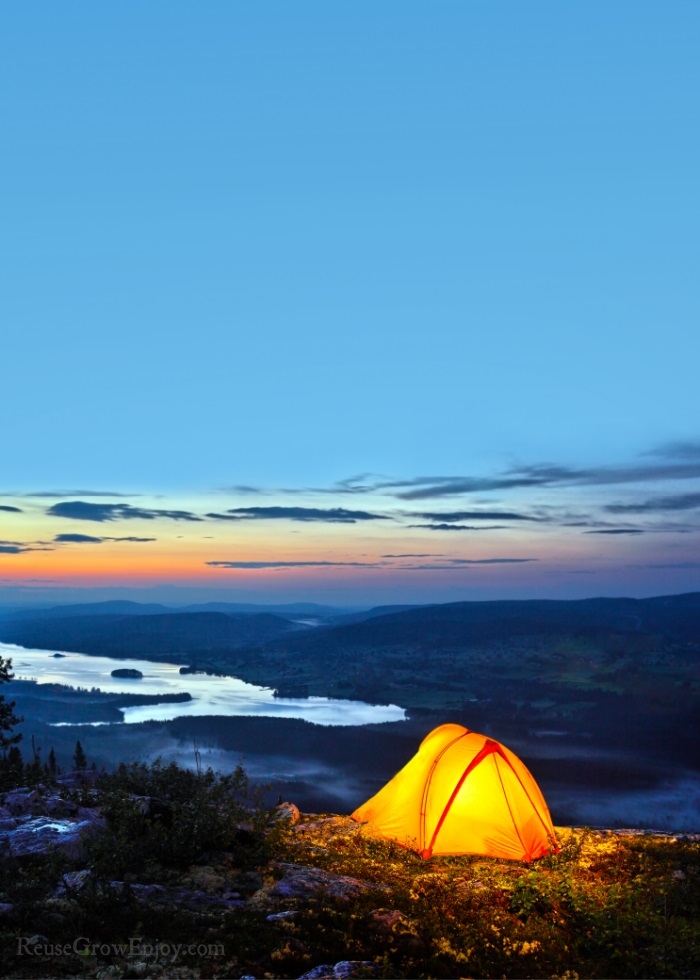 Tent at night with light inside on side of hill over looking a river