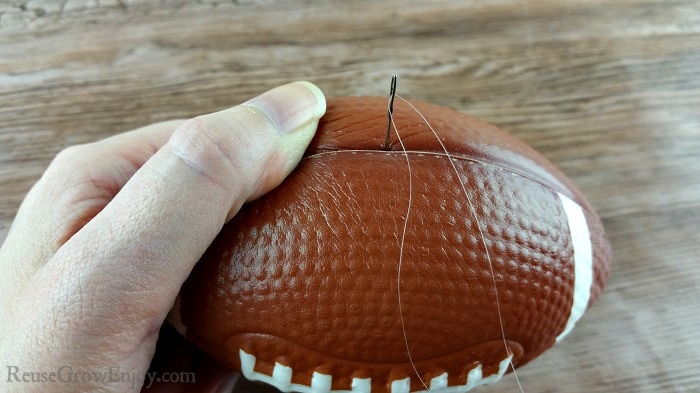 A needle with clear thread being pushed through a foam football.