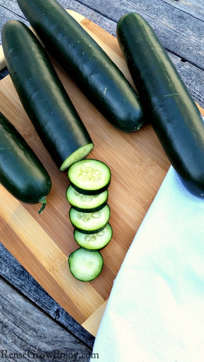 Fresh garden cucumbers on a wood cutting board with one half sliced up - Tips On How To Grow Cucumbers