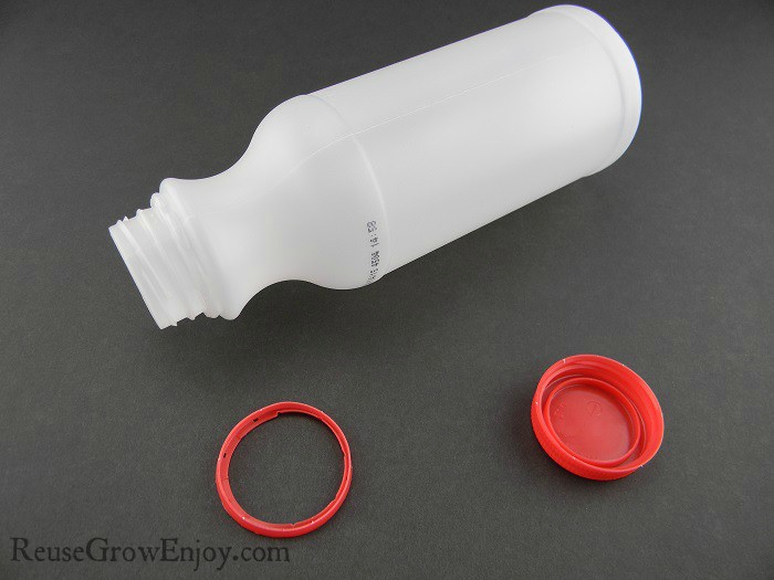 Small empty plastic milk bottle with top and ring removed on black background