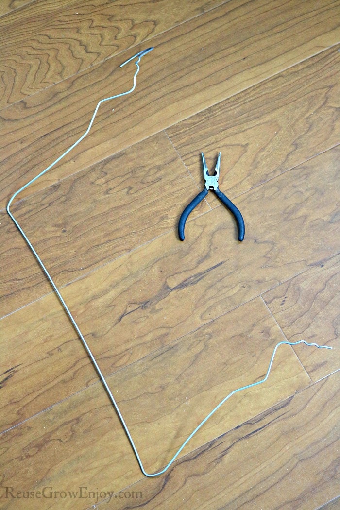 Coat hanger un twisted with pliers laying next to it