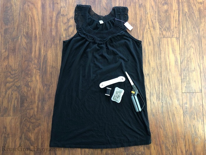 Small black tank style dress on wood floor with scissors, thread, pins and elastic laying on top of it.