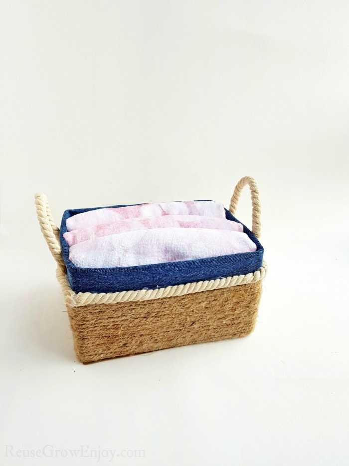 Small rope basket with rope handles full of folded cloth.