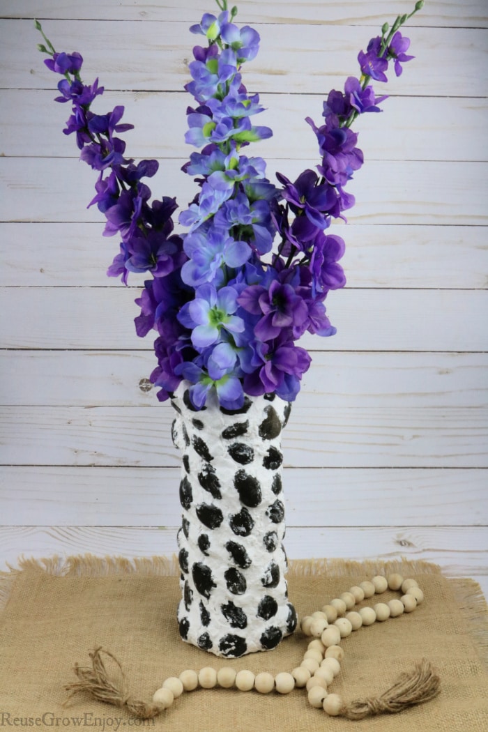 Upcycled Chip Can Into Stone Vase With purple flowers in vase and wood beads at base