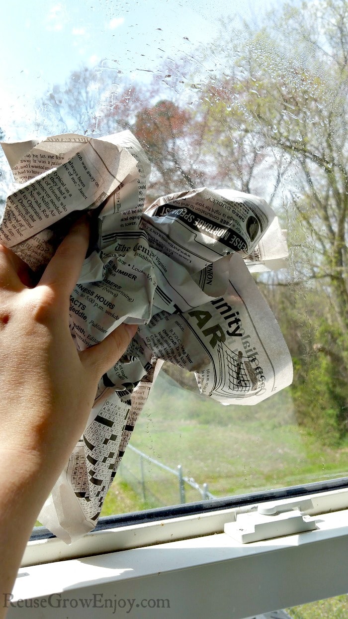 Hand holding bunched up newspaper wiping the window with it.