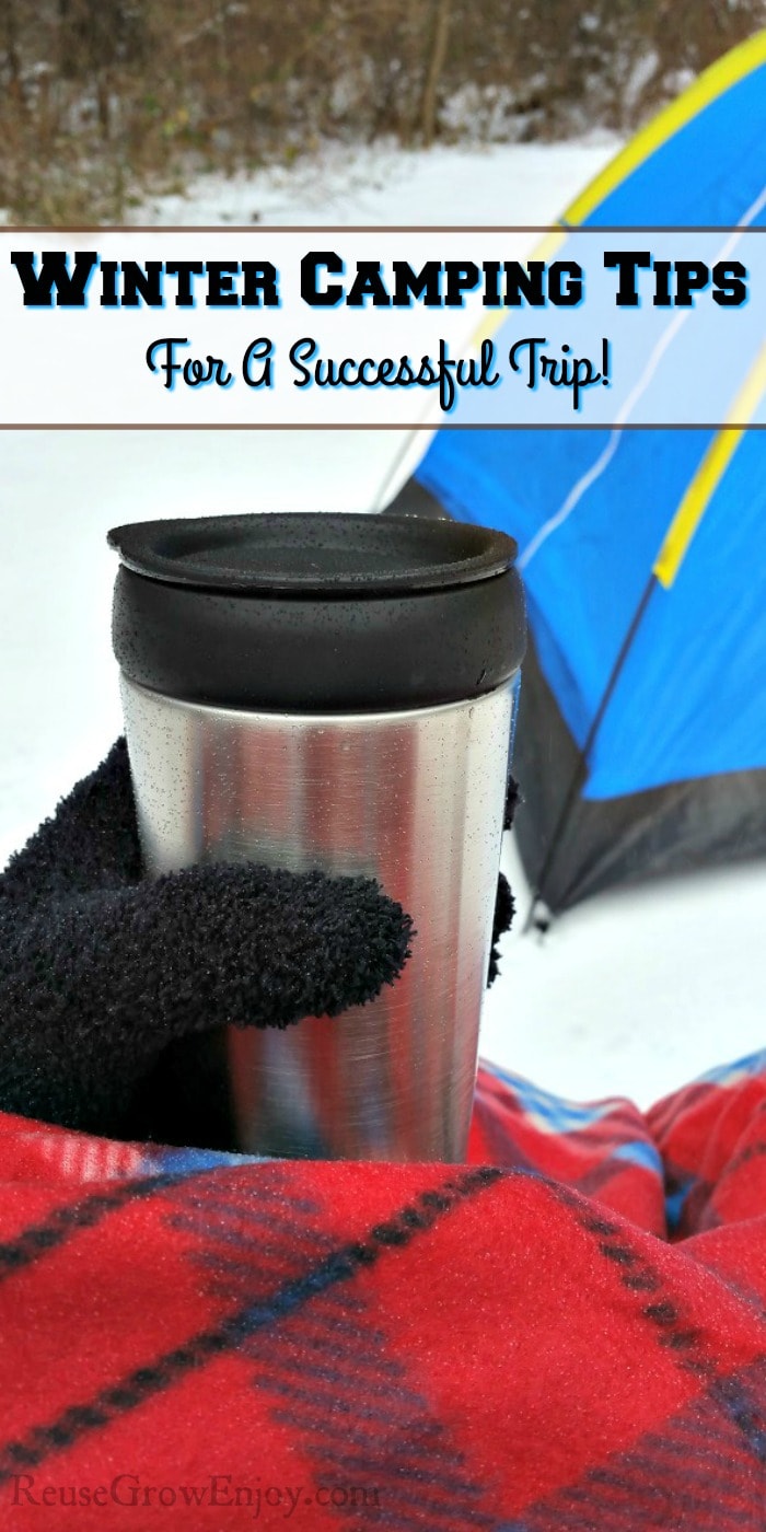 Snow on ground with tent in the background and a hand with a black glove holding a stainless steel mug and covered in red plaid blanket with a text overlay that says "Winter Camping Tips For A Successful Trip".